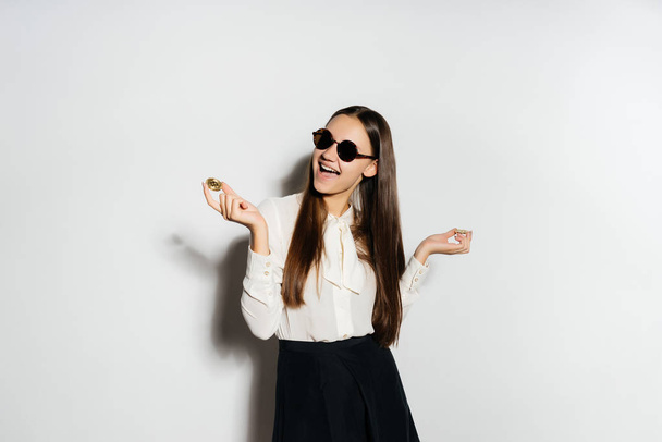 happy girl in black glasses holds a coin on a white background - Valokuva, kuva