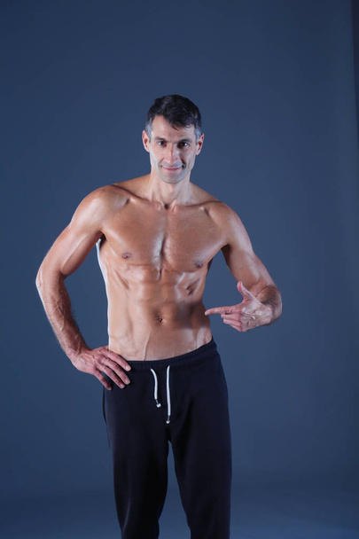 muscular man. Muscular man on a grey background showing muscles. Fitness instructor. Fitness professional. Workout. Mens fitness. - Valokuva, kuva
