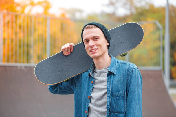 Young skatebarder posing with skateboard in the skatepark. Sport concept. - Zdjęcie, obraz
