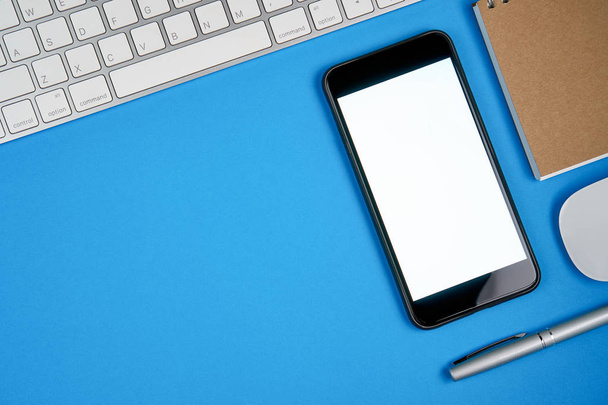 Smartphone de pantalla negra en blanco y teclado con bloc de notas colocado sobre fondo azul. Adecuado para gráficos utilizados para publicidad
. - Foto, imagen