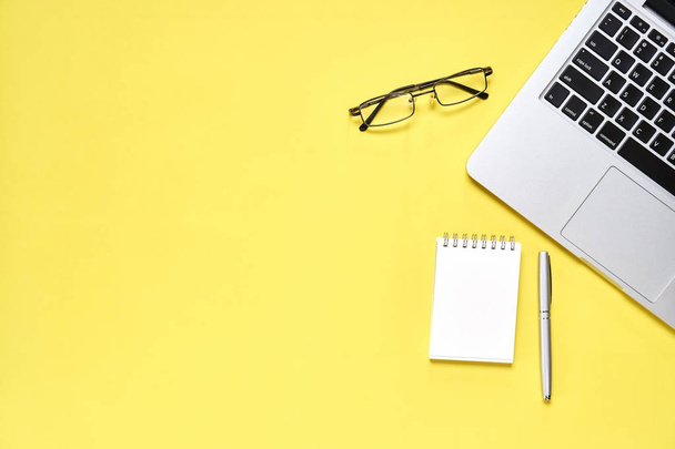 Bovenaanzicht, moderne werkplek met laptop en notebook met pen op een pastel gele achtergrond geplaatst. Ruimte geschikt voor gebruik in afbeeldingen kopiëren. - Foto, afbeelding