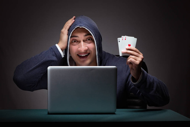 Giovane uomo che indossa una felpa con cappuccio seduto davanti a un computer portatile - Foto, immagini
