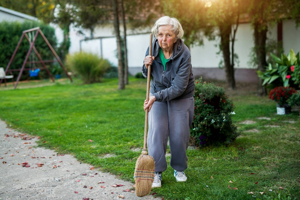Starší žena s koštětem na dvorku - Fotografie, Obrázek