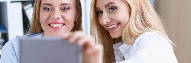 Two businesswomen in the office smile and do selfie - Photo, Image