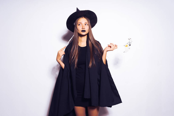 a young sexy gothic girl dressed as a witch for Halloween, holds a magic wand and looks thoughtfully upwards - Fotografie, Obrázek