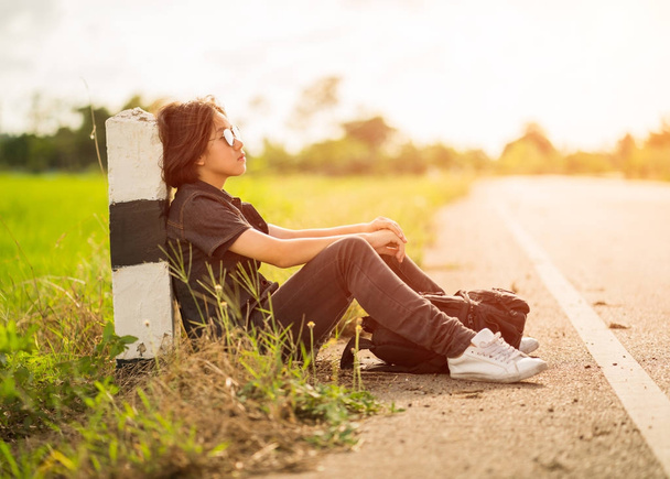 Woman sit with backpack hitchhiking along a road in countryside - Foto, Imagen