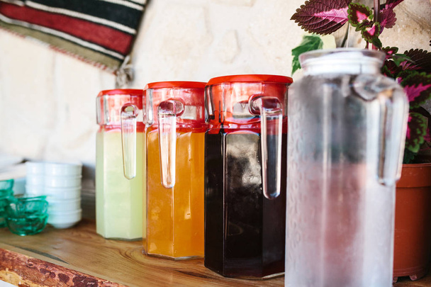 Glaskrüge mit verschiedenen Obst- und Beerengetränken mit roten Deckeln stehen auf dem Tisch - Foto, Bild