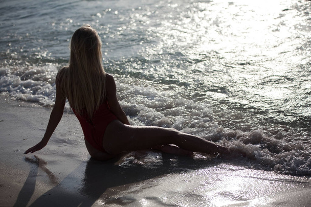 Sexy girl lies in a red swimsuit near the ocean. Back view. - Fotoğraf, Görsel