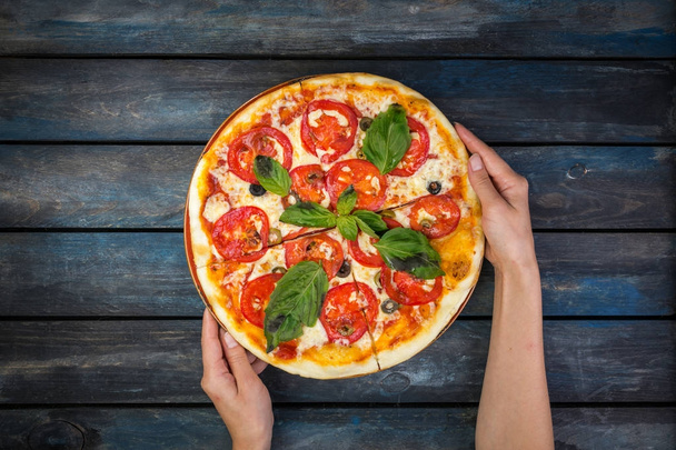 Womans ręce trzymając perfekcyjny pizza margarita z plastrami pomidorów, oliwek i bazylii liści. Widok z góry - Zdjęcie, obraz