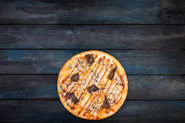 Delicious pizza with mushrooms chicken meat and onions on a dark wooden background. Top view bottom orientation - 写真・画像