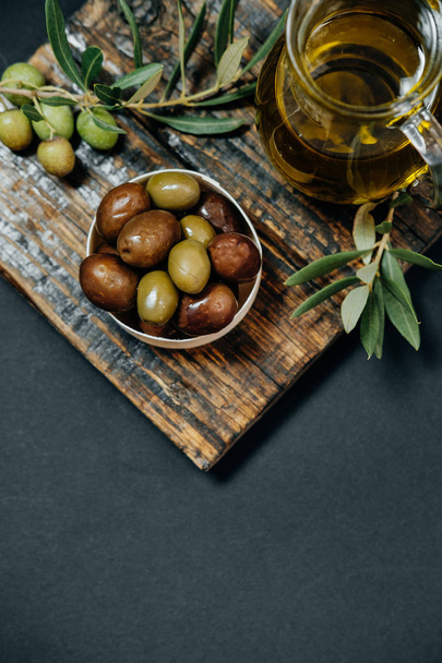 Top view Olives, oil and green branch on black background - Фото, изображение
