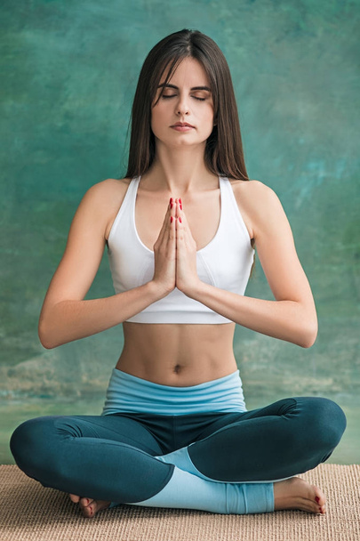Studio shot of a young woman doing yoga exercises on green background - Photo, image