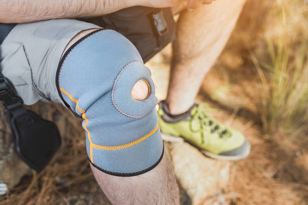 Close up van knie steunbeugel op been van een reiziger man tijdens het wandelen buiten in de natuur - Foto, afbeelding