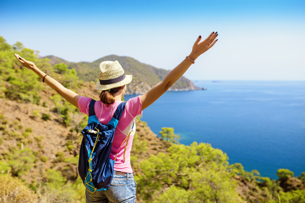 Молодая женщина путешественник с рюкзаком стоя на краю скалы и глядя на средиземноморский морской пейзаж, летние каникулы концепции
 - Фото, изображение