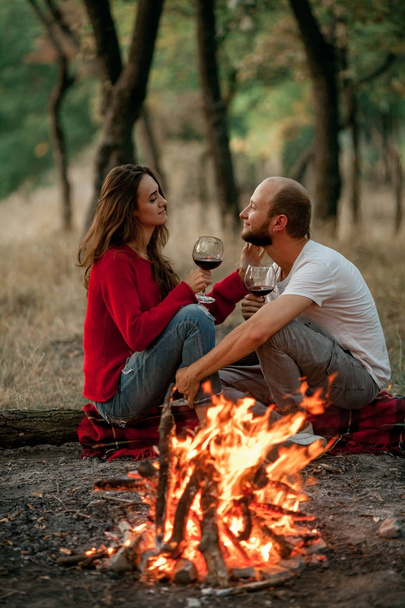 Enamored couple sits on picnic in forest on bonfire flame background. - Foto, imagen