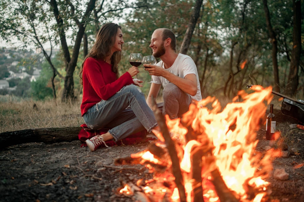 Couple amoureux assis et sourires sur le pique-nique dans la forêt sur fond de flamme de feu de joie
. - Photo, image
