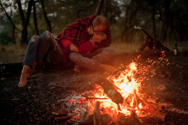 Enamored couple lies, hugs and kisses in forest against background of bonfire flame. - Photo, Image