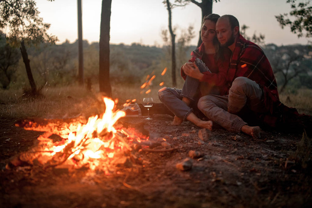 Enamored couple sits on picnic on background of bonfire flame. - 写真・画像