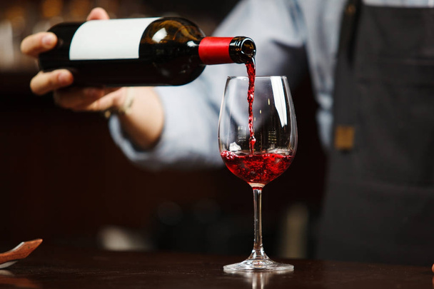 Waiter pouring red wine into wineglass. Sommelier pours alcoholic drink - Zdjęcie, obraz
