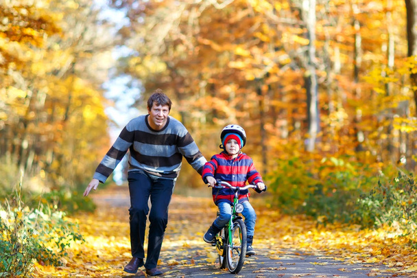 Little kid boy and his father in autumn park with a bicycle. Dad teaching his son biking - Photo, Image