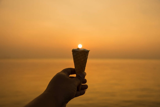 Uomo mano tenendo gelato alla vaniglia cono all'ora d'oro tramonto ba
 - Foto, immagini