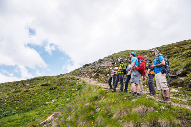 A group of hikers with backpacks and tracking sticks rest and stands in the mountains listening to their guide - Zdjęcie, obraz