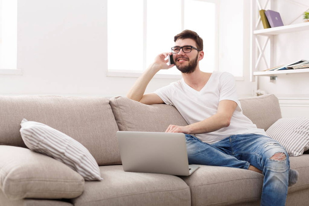 Glimlachend jonge man thuis met laptop en mobiele - Foto, afbeelding