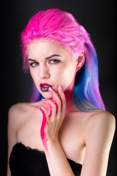 Portrait of attractive young woman with painted colorful hair. Half-length standing and touching face by hand. Dark background. - Photo, image