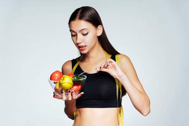 siyah spor top bir güzel ince kız onu rakam saatler, bir tabak yararlı sebze ve meyve ve bir çatal ile almıştır - Fotoğraf, Görsel