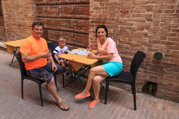 de familie zit aan de tafel van een café in de smalle straat van Italië. - Foto, afbeelding