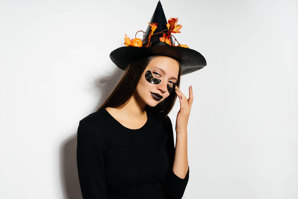 a young gothic sexy girl with pale skin, a big black hat on her head, adorned with yellow leaves, on her lips a black lipstick - Photo, Image