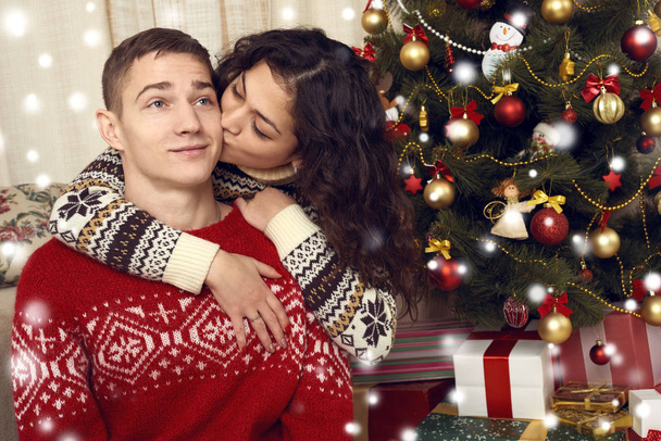 幸せなカップルは、自宅のクリスマスの装飾でキスします。大晦日、ornated モミの木。冬の休日や愛の概念. - 写真・画像