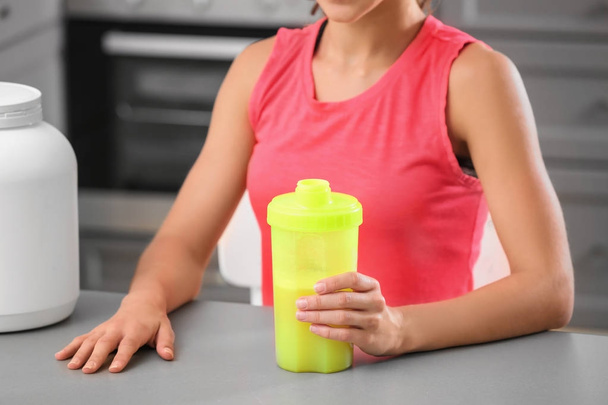 Young woman holding bottle with protein shake indoors - Photo, image