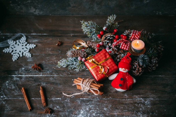 Composição clássica de Natal e Ano Novo. Caixa de presente com velas, boneco de neve, cones de pinho, em fundo de madeira
 - Foto, Imagem