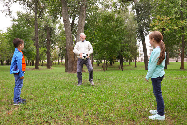 Senior man and his grandchildren playing with ball in park - Фото, зображення