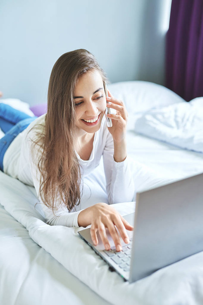 Młoda kobieta uśmiechający się z laptopa za pomocą telefonu - Zdjęcie, obraz