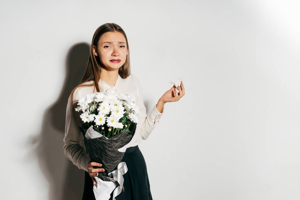a young girl in a white shirt is holding a bouquet of white flowers and sneezes because she is allergic - Foto, Bild