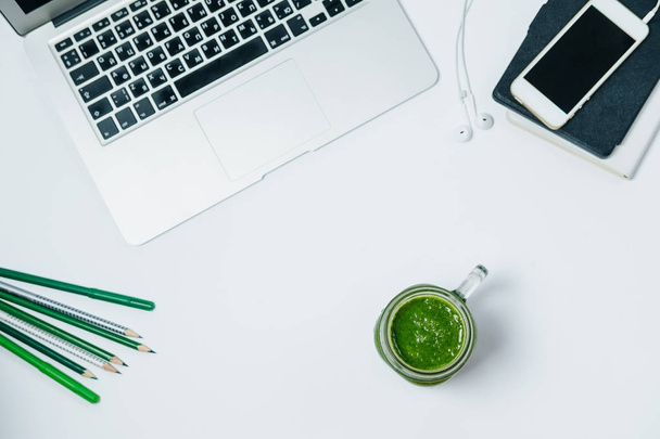 Healthy work space with green smoothie and laptop on white backg - Photo, image