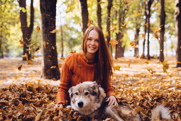 beautiful laughing red-haired girl playing with her dog in fallen autumn leaves - Foto, immagini