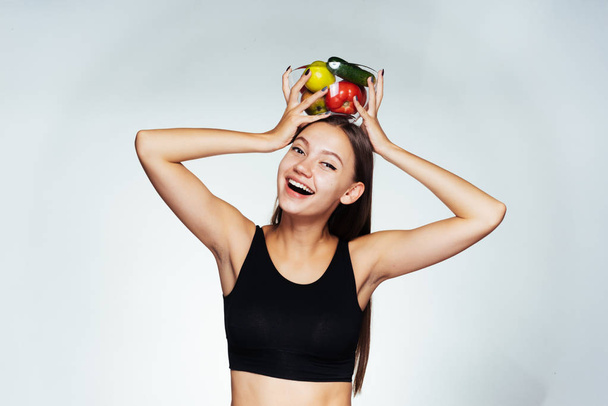 happy laughing sports girl in a black top holding a plate with useful vegetables and fruits - Photo, Image