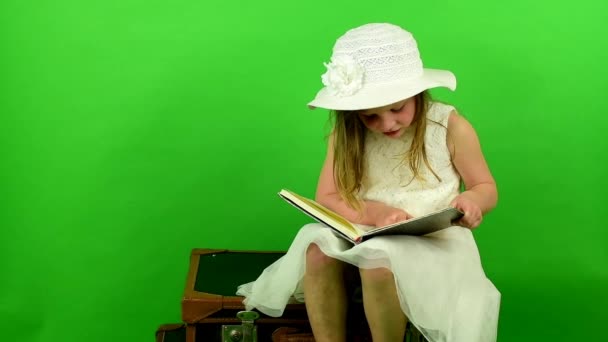 Κορίτσι κάθεται σε βαλίτσες και διαβάζει το βιβλίο. Κορίτσι smalll στο chroma κλειδί φόντο. Ταξιδεύοντας έννοια. - Πλάνα, βίντεο