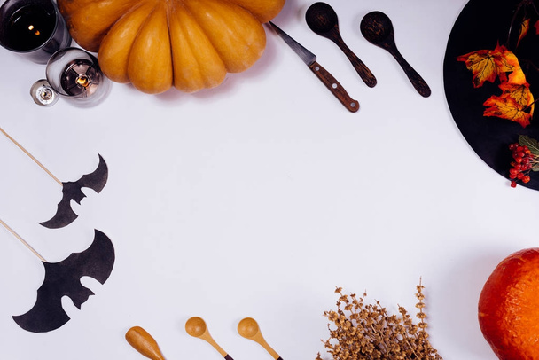 on a white table lie orange pumpkins, burning scented candles, lie wooden spoons, yellow autumn leaves - Fotó, kép