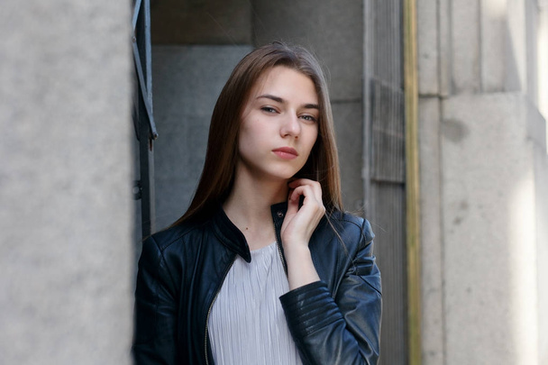 Young beautiful woman in dress and leather jacket standing at roof near fence - 写真・画像