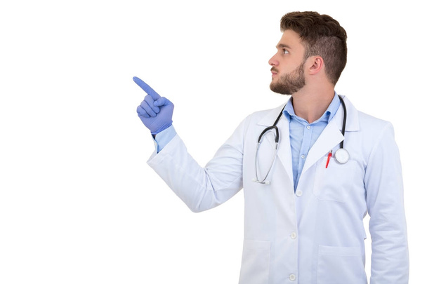 Portrait of a smiling male doctor pointing finger away isolated on a white background - Foto, Imagen