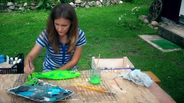Νεαρός καλλιτέχνης γυναίκα ζωγραφική διακόσμηση ψάρια στο ξύλινο τραπέζι στην αυλή του σπιτιού - Πλάνα, βίντεο