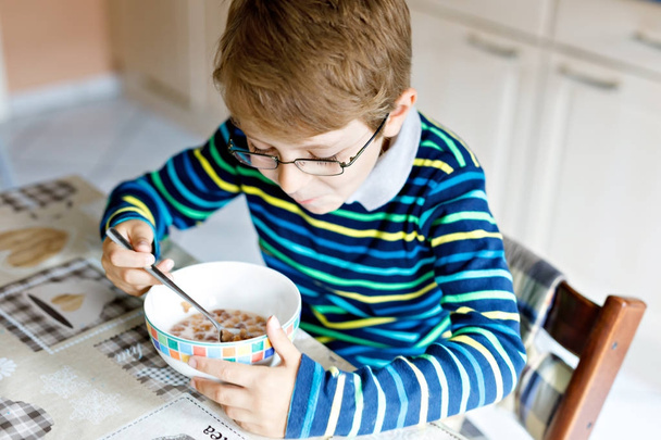 Happy little blond kid boy eating cereals for breakfast or lunch. Healthy eating for children. - Photo, Image