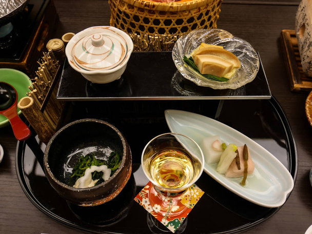 桜豆腐、ユリ球根豆腐、馬の尾、マタタビとゴマ、アンコウの肝のムース、他のおかずと梅酒を含む旅館懐石ディナー前菜 - 写真・画像