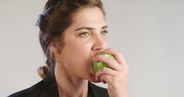 Woman eating an apple on a white studio background - Felvétel, videó