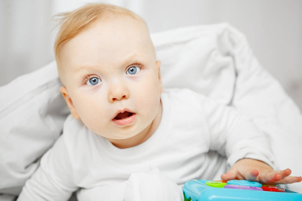 Cute baby sits on bad under blanket with toy - Photo, image