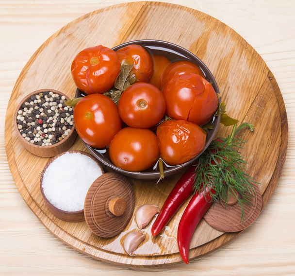 Los tomates salados en el plato, sobre la tabla de madera y el condimento
 - Foto, imagen